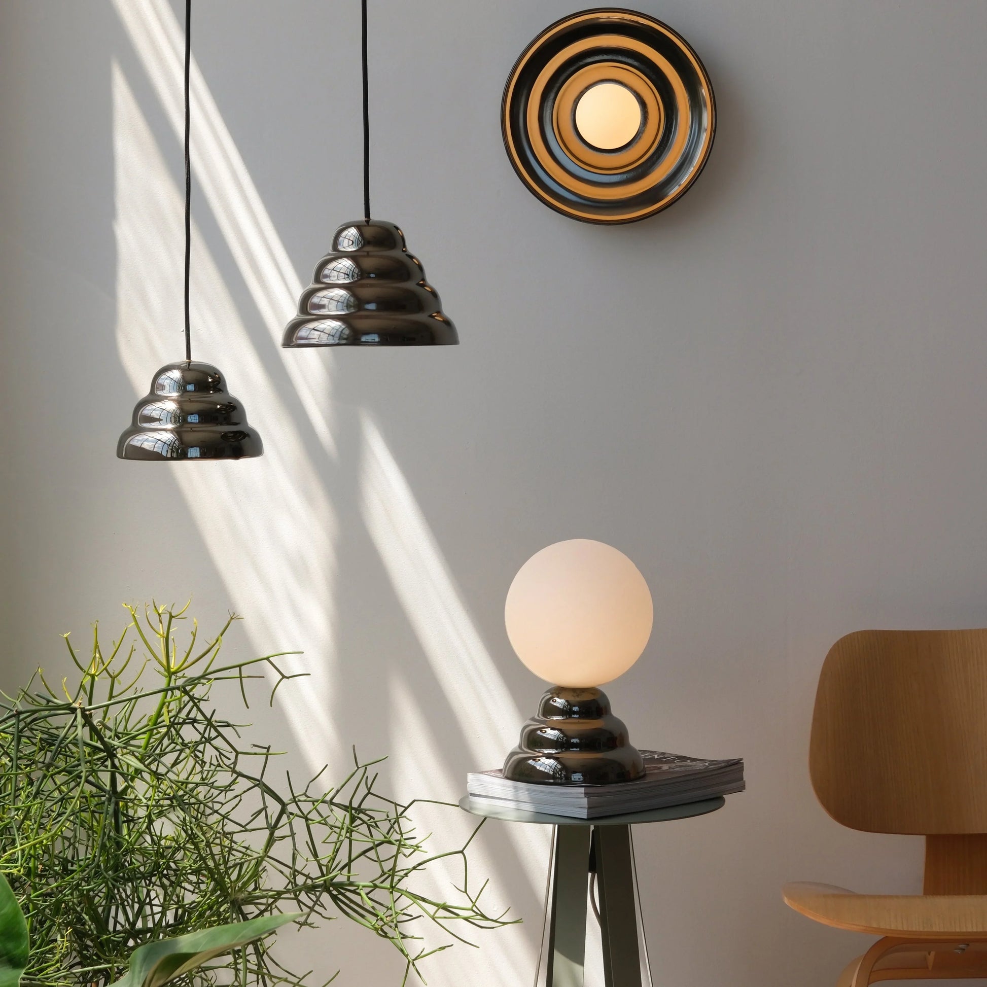 Modern ceramic pendant lights hanging beside a matching concentric wall sconce and a glass globe table lamp on a minimalist side table near a wood accent chair
