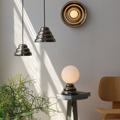 Modern ceramic pendant lights hanging beside a matching concentric wall sconce and a glass globe table lamp on a minimalist side table near a wood accent chair