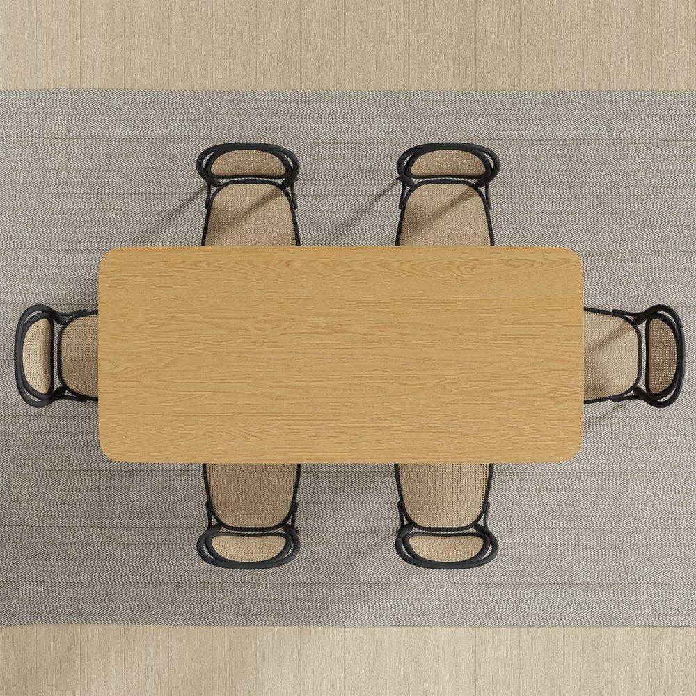 Top down birds eye view of a rectangular natural oak double pedestal dining table arranged with six woven cane chairs on a textured herringbone area rug
