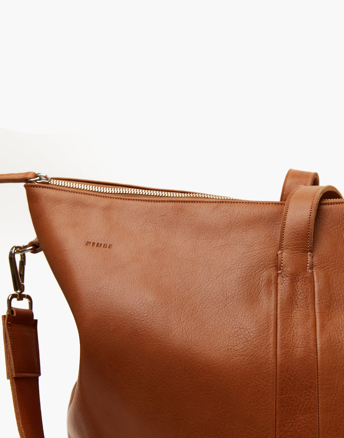 Close-up of the Malbec weekender in Tobacco, showing leather grain, embossed Nimes branding, top zipper, and strap attachment.
