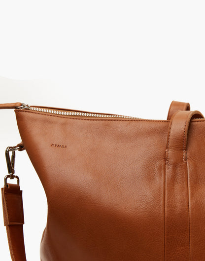 Close-up of the Malbec weekender in Tobacco, showing leather grain, embossed Nimes branding, top zipper, and strap attachment.