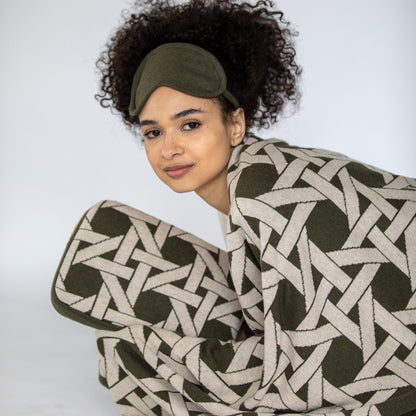 Woman wrapped in olive green geometric organic cotton travel blanket wearing matching eye mask close up detail