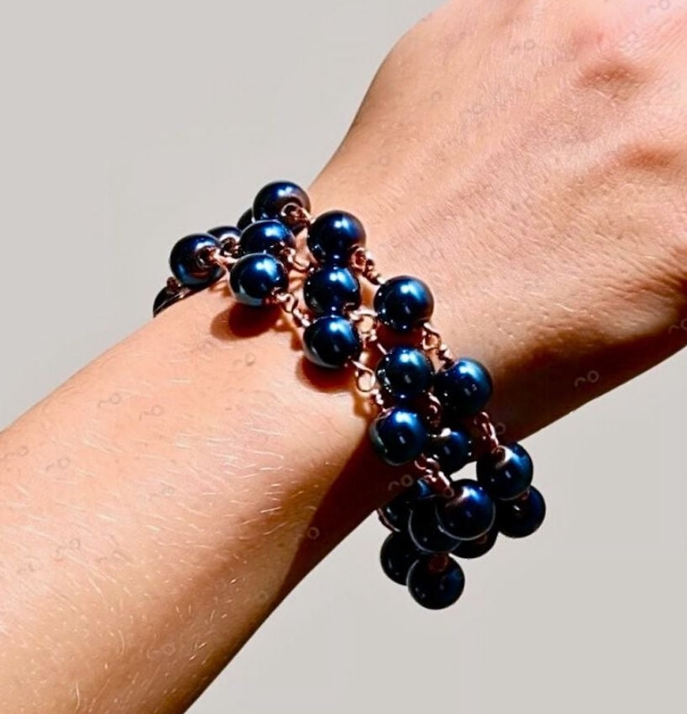 Close-up of Celeste blue hematite artisan bracelet worn on a wrist, showing three strands of reflective dark blue beads and rose-gold-tone wire connections.