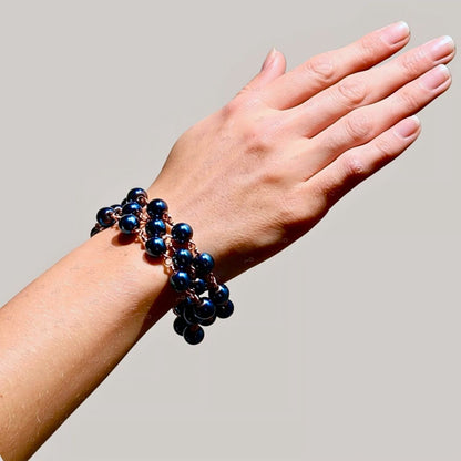 Celeste blue hematite artisan bracelet worn on a wrist, showing three strands of dark shimmering blue beads linked with rose-gold-tone wire.