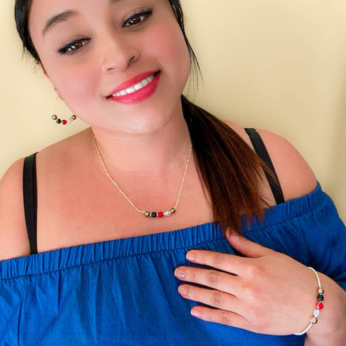 Model wearing the His-Story Majorca pearl bangle bracelet with coordinating necklace and earrings, styled with a blue off-the-shoulder top.