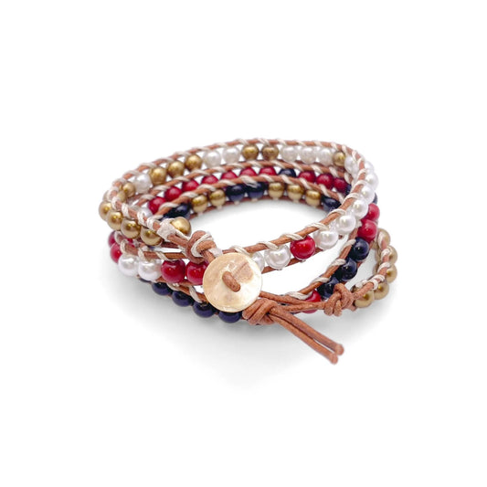 Majorca pearl wrap bracelet with black, red, gold, and white beads, tan leather cords, silk threadwork, and a mother of pearl button on a white background.