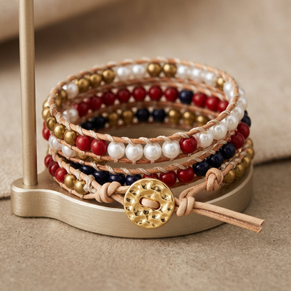 Multicolored pearl wrap bracelet with tan leather cords and white, red, dark, and gold-tone beads, arranged around a display stand with a textured gold-tone button.