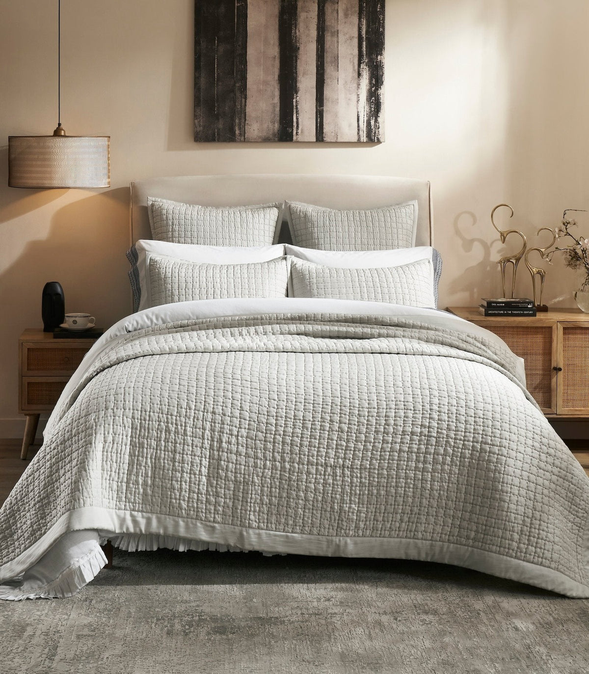 Malibu Mist quilted silk coverlet in a pale gray tone, showing square stitching and a smooth border on a bed between wooden nightstands