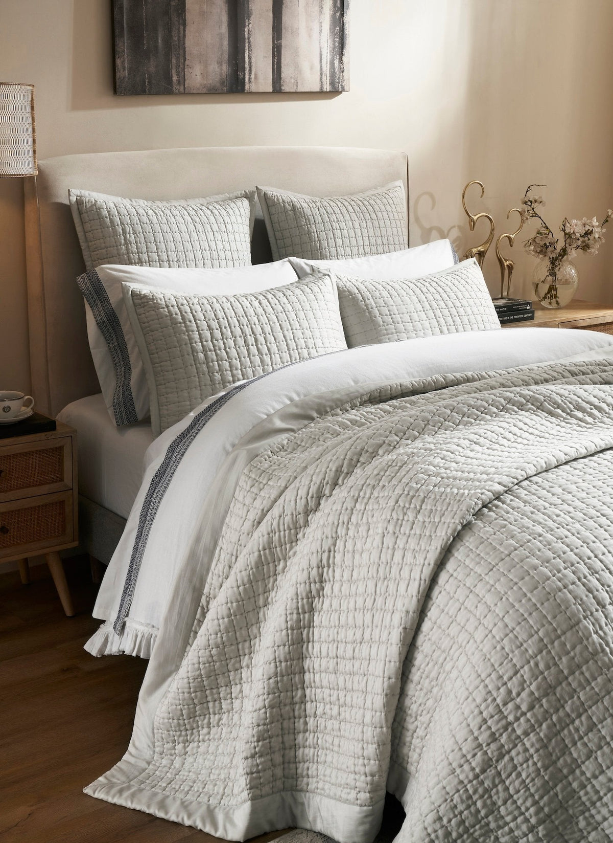 Malibu Mist quilted silk coverlet folded back across a bed, highlighting its pale gray sheen, square stitching, and smooth border, with coordinating pillows behind.