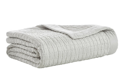 Malibu Mist quilted silk coverlet folded on a white background, showing its pale gray tone, textured square stitching, and smooth border.