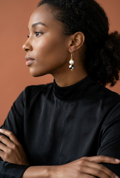 Model wearing a Sefone drop earring with a cream bead, black-and-white patterned bead, and gold-tone accents, paired with a black high-neck top.