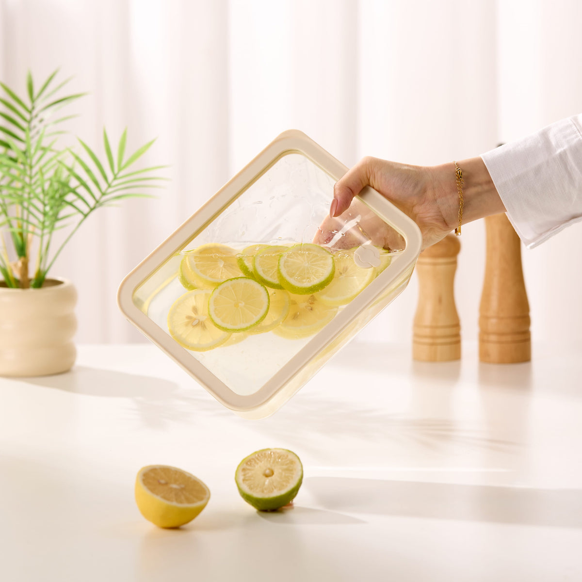 Premium glass food storage container held by hand filled with fresh lemon slices in a bright modern kitchen with indoor plant and wood accents