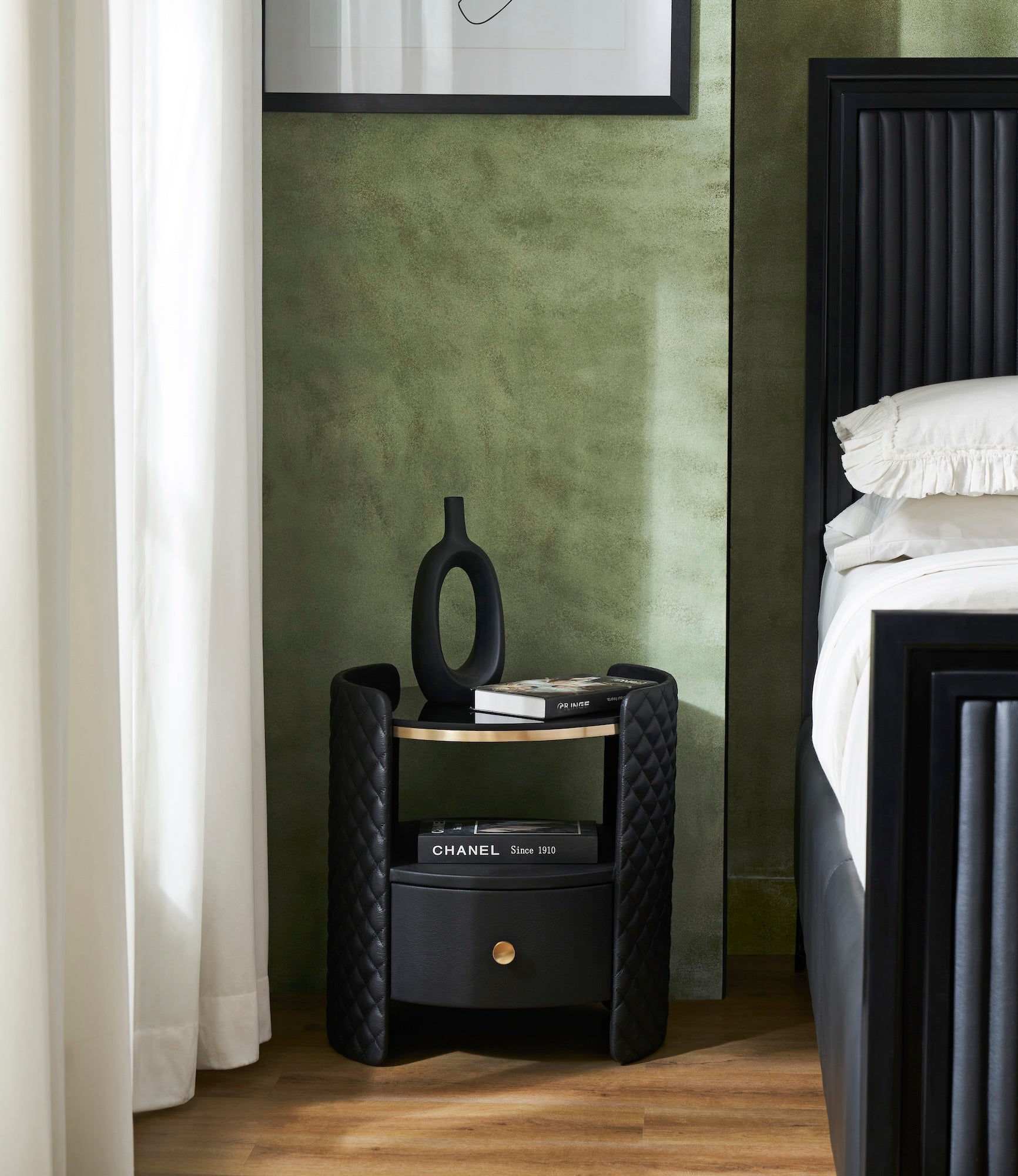 Quilted Round Leather Nightstand black bedroom lifestyle beside bed sculptural vase Chanel book green wall 