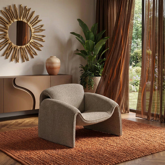 Sculpted taupe boucle lounge chair with curved arms on a rust-colored rug beside floor-to-ceiling windows
