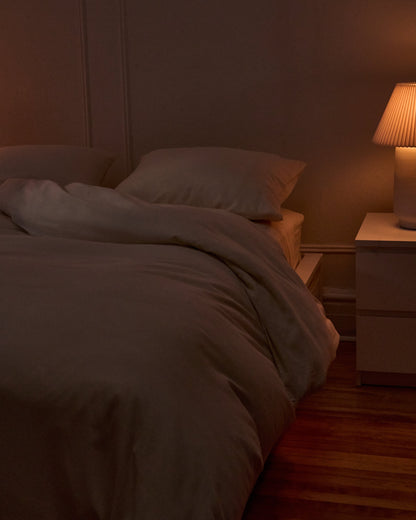 Signature Milk Fibre Deluxe Set Cream duvet cover and pillowcases on a bed in a warm evening bedroom setting