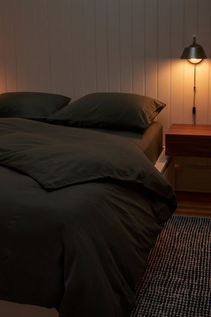Signature Milk Fibre Deluxe Set Highlands Green duvet cover and pillowcases on a bed in a warm ambient bedroom with pendant wall lamp and wood nightstand