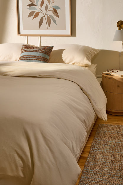 Signature Milk Fibre Duvet Cover Cream on a styled bed with warm neutral bedroom setting and botanical wall art