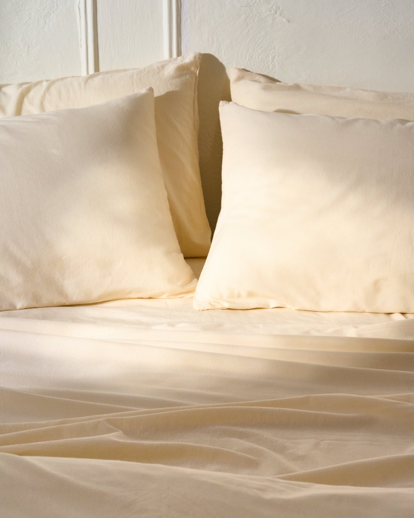 Signature Milk Fibre Sheet Set in Cream styled on bed with pillows in warm natural light
