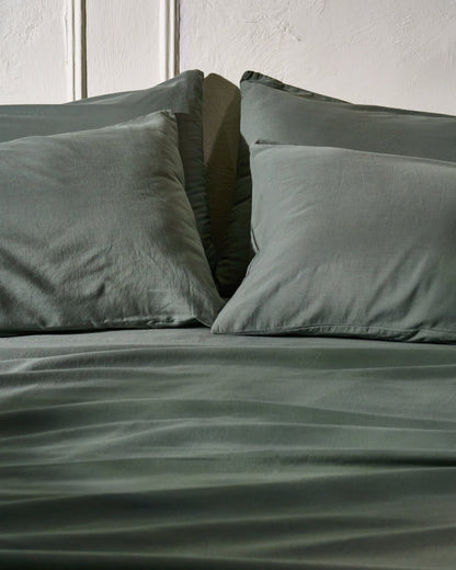 Signature Milk Fibre Sheet Set in Highlands Green two pillows styled on bed with textured wall background