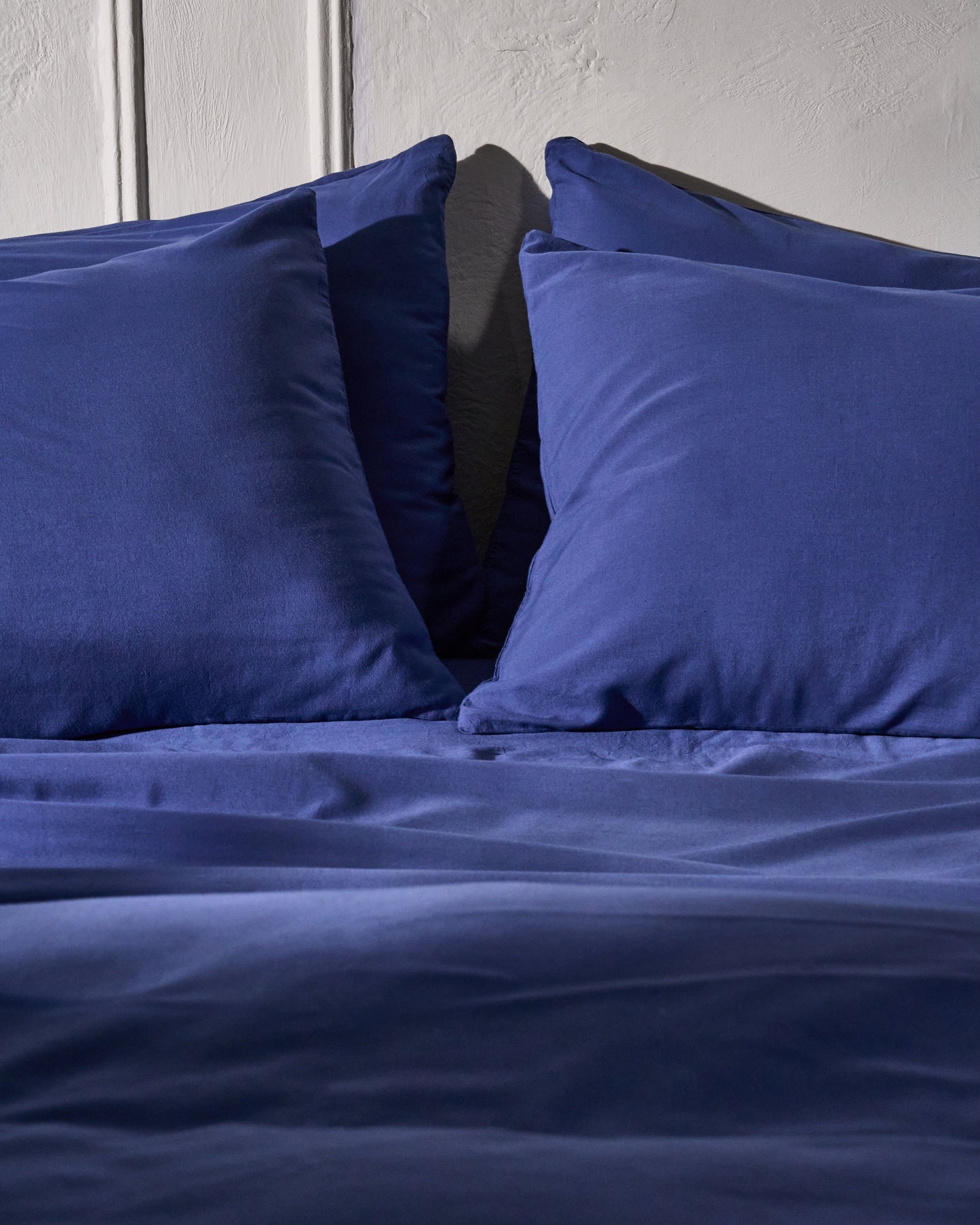 Signature Milk Fibre Sheet Set in Lunar Blue two pillows styled on bed with textured wall background