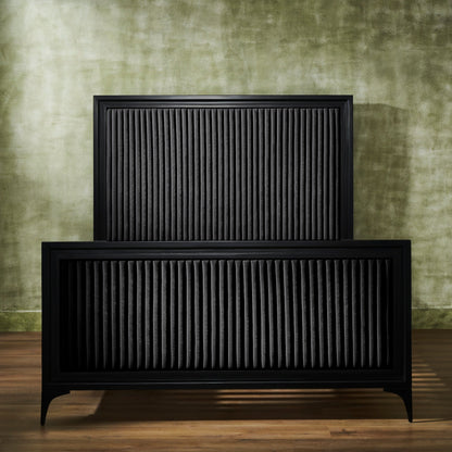 Front-facing view of a black genuine leather quilted bed frame showing full panel headboard and footboard with vertical stripe quilting, iron legs, against a green textured wall on hardwood floor. 🌿