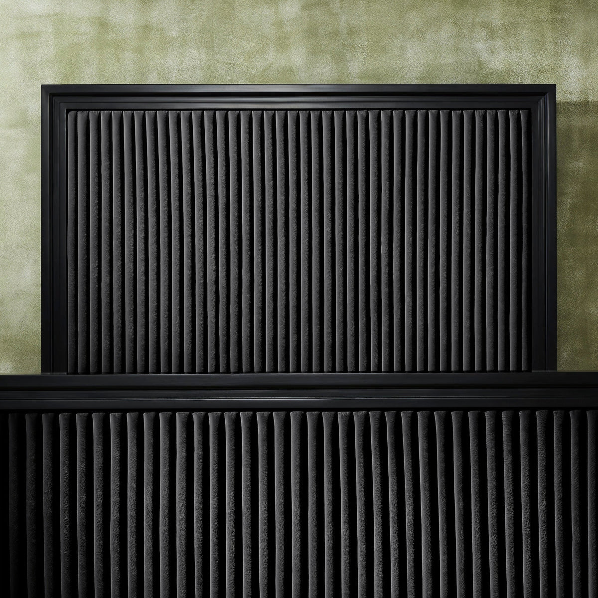 Front-facing close-up of black genuine leather quilted panel headboard and footboard showing vertical stripe quilting detail and matte black frame border against a green textured wall. 🌿