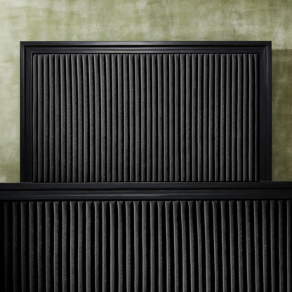 Front-facing close-up of black genuine leather quilted panel headboard and footboard showing vertical stripe quilting detail and matte black frame border against a green textured wall. 🌿