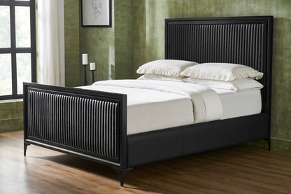 A black genuine leather quilted bed frame styled with white bedding and pillows, vertical stripe quilting on panel headboard and footboard, iron legs, in a modern bedroom with green walls, hardwood floor, and natural window light. 