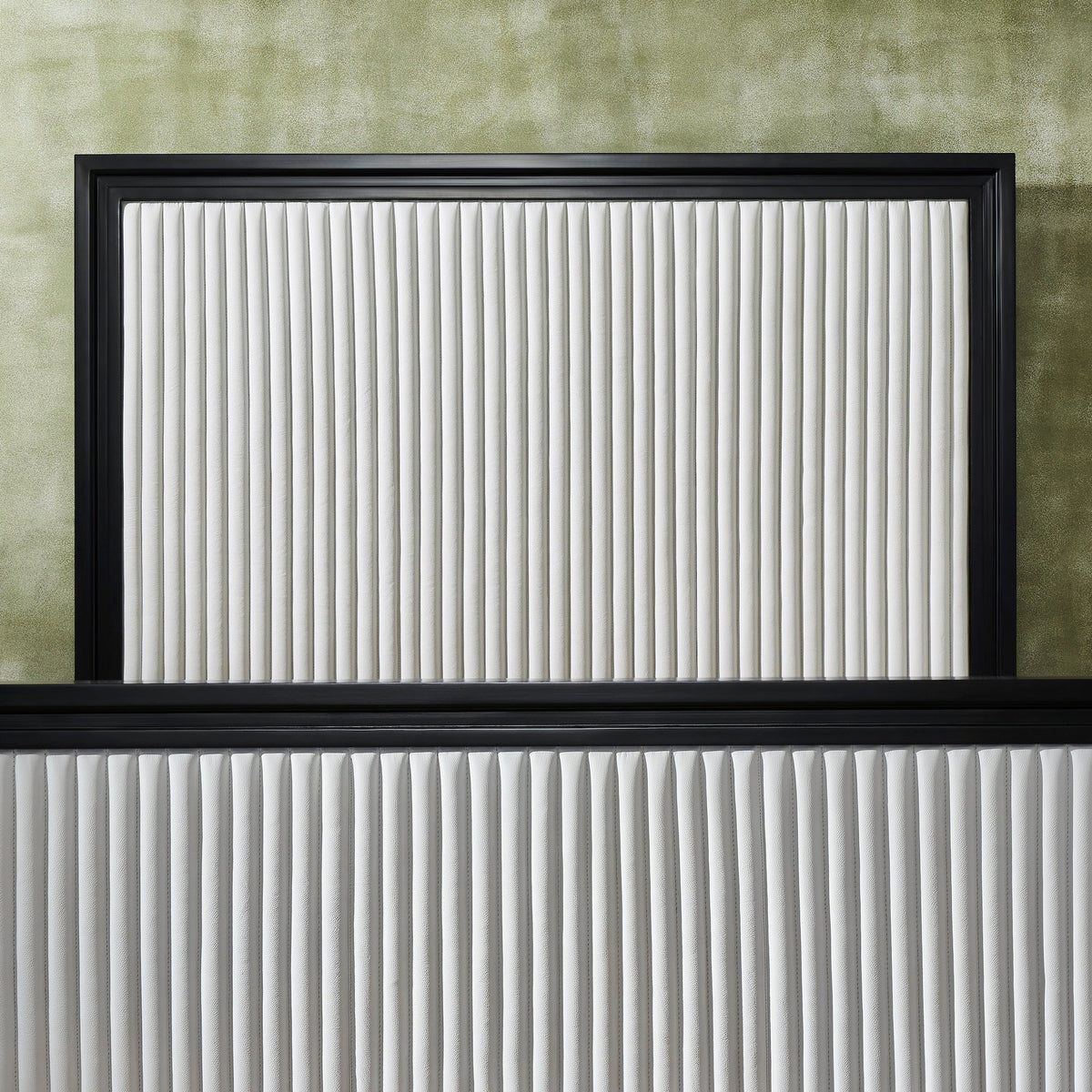 Close-up detail of a white genuine leather quilted bed frame showing vertical stripe quilting texture on panel headboard and footboard with black frame border, against a green textured wall. 🌿