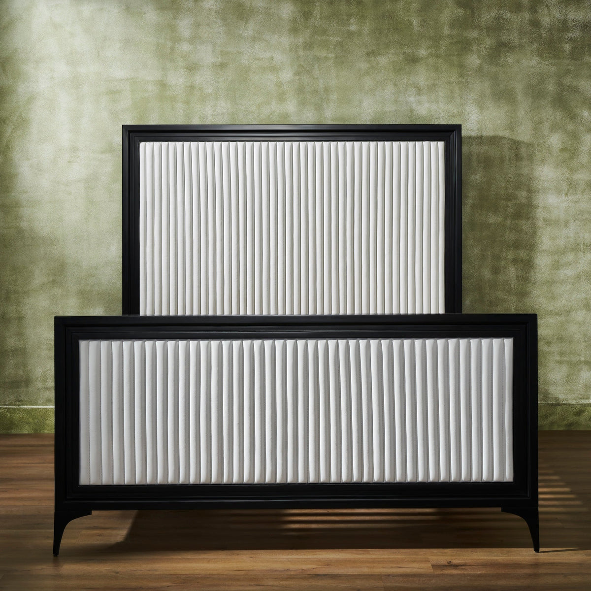 Front-facing view of a white genuine leather quilted bed frame with vertical stripe quilting, black matte frame border on panel headboard and footboard, iron legs, against a green textured wall on hardwood floor. 🌿