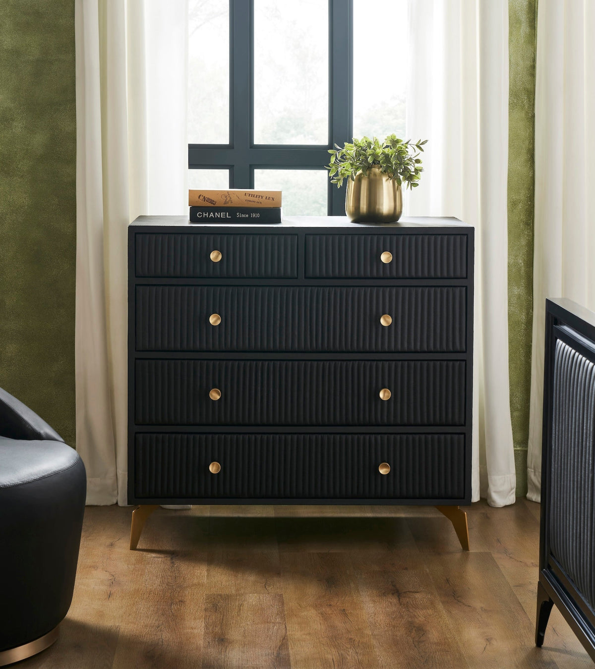 Stanford Ribbed Five-Drawer Leather Chest in black genuine leather styled with a brass vase, coffee table book, and sage green wall in a modern bedroom setting