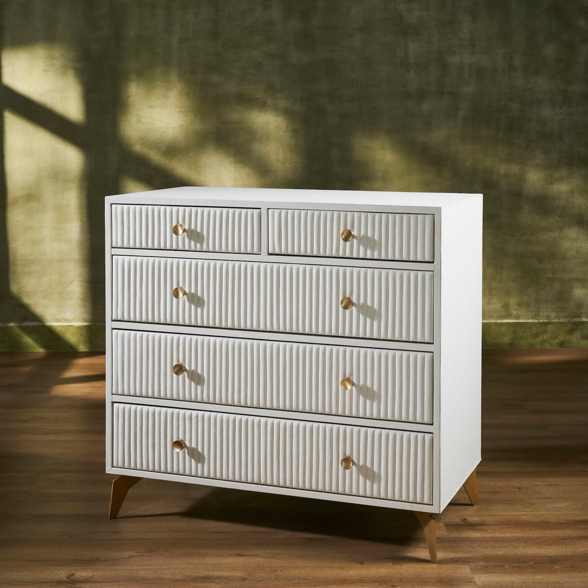 Stanford Ribbed Five-Drawer Leather Chest in white genuine leather at three-quarter angle showing ribbed drawer fronts, brass knobs, and angled brass legs