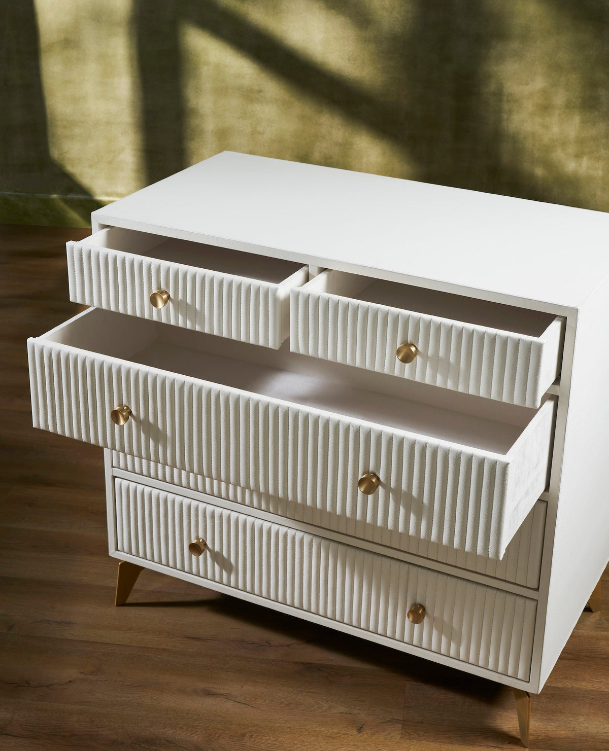 Stanford Ribbed Five-Drawer Leather Chest in white with top drawers open showing smooth micro-suede lined interiors and brass knobs on angled brass legs