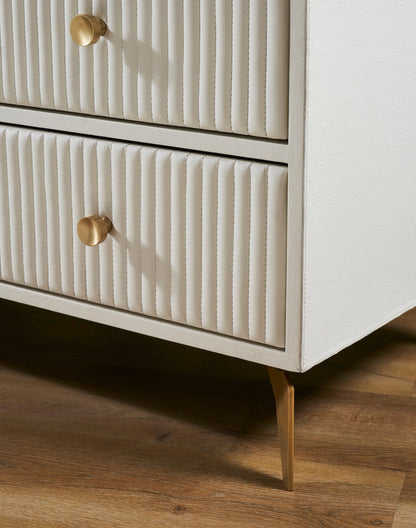 Close-up of angled brass leg and lower ribbed genuine leather drawer fronts with solid brass knobs on the Stanford white leather chest