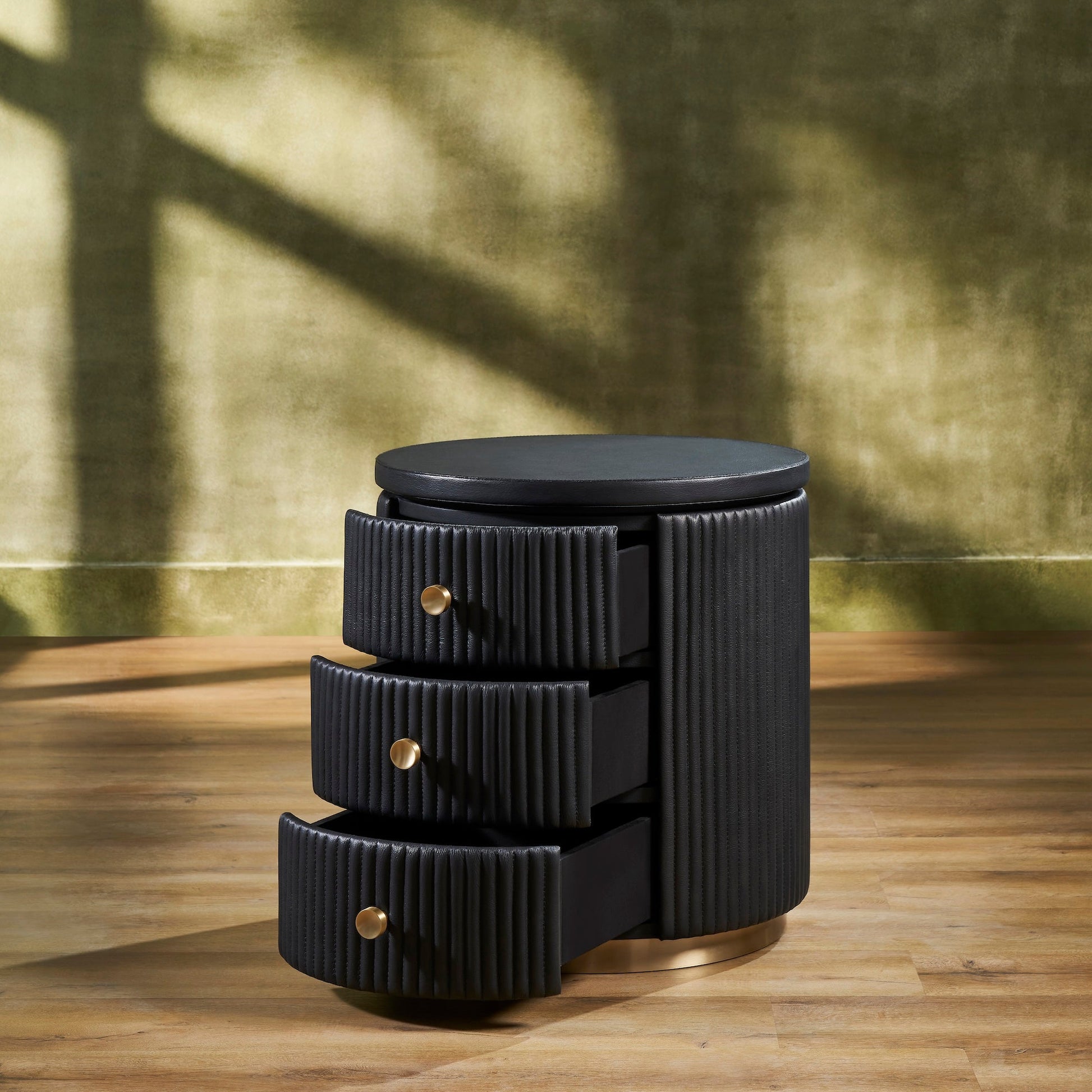 Stanford Round Fluted Leather Nightstand black three drawers open brass knobs brass rim base angled view golden wall hardwood floor