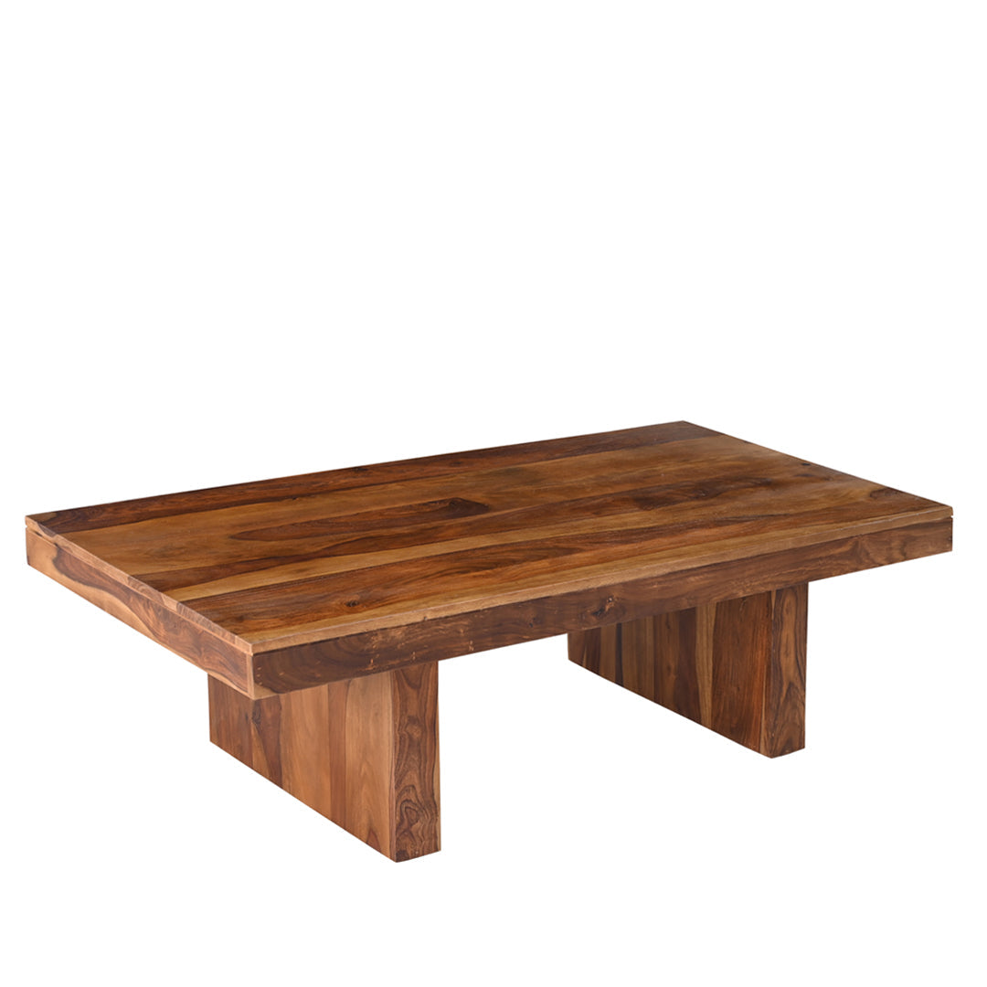 Solid seesham wood coffee table at an angle showing thick plank top and wide block base legs, natural grain pattern and warm brown finish visible across the surface