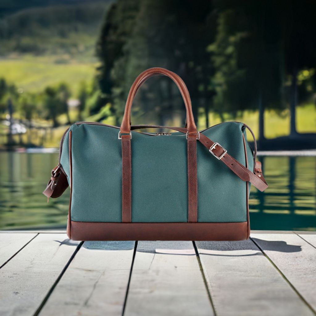 Wanderlust Weekender canvas duffel Classic Green evening lifestyle shot on wooden surface with ambient light highlighting structured silhouette and leather trim