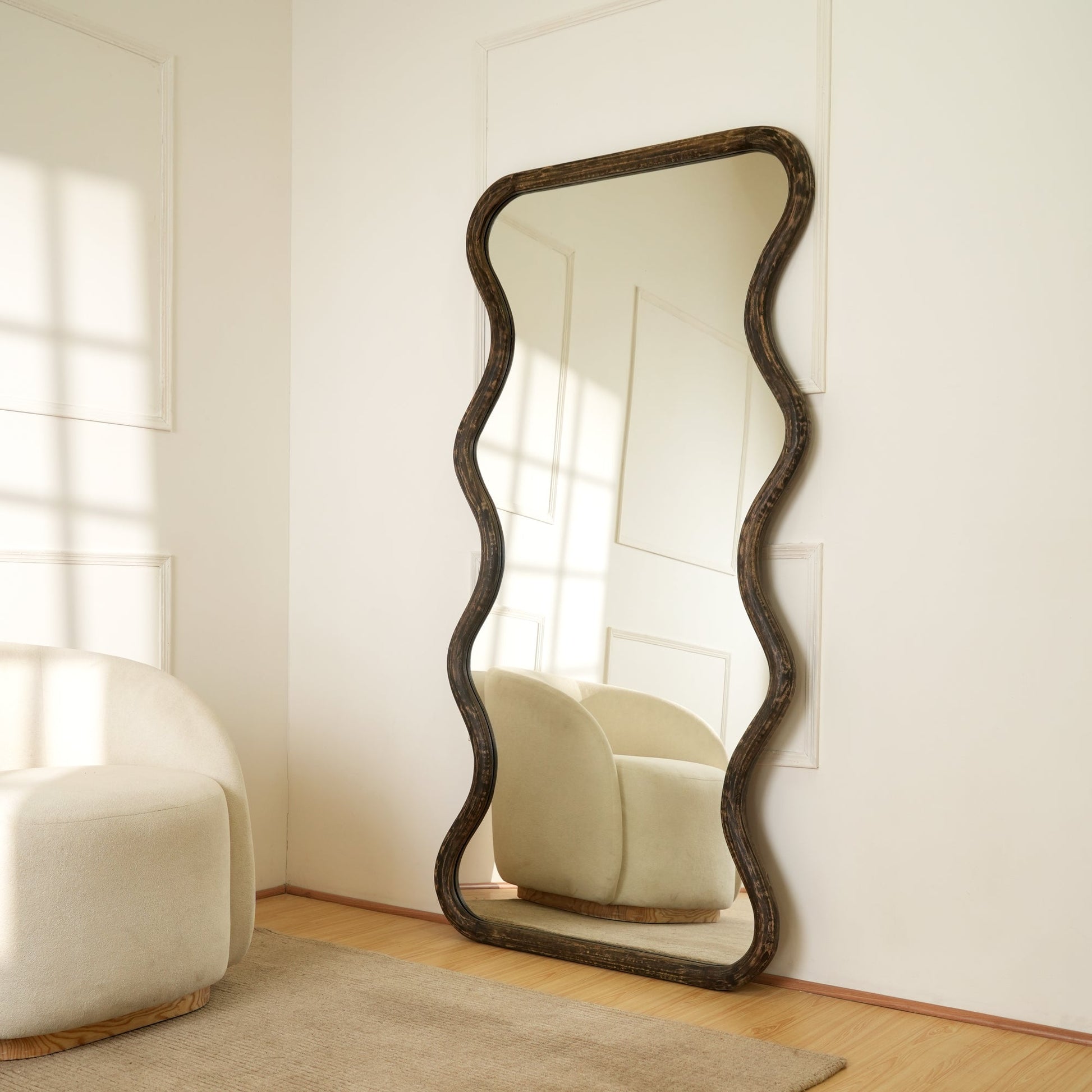 Wavy mango wood wall mirror styled in a bright living room corner beside a cream bouclé chair reflecting natural window light

