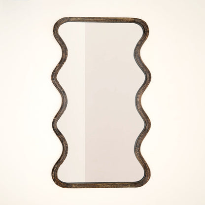 Wavy mango wood wall mirror with sculptural wave silhouette and brown antique finish against a neutral white background

