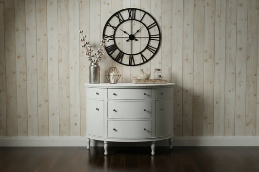 A farmhouse-styled lifestyle view of the White Demilune Console Chest set against a rustic wood-planked wall with a large decorative wall clock.