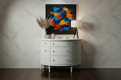 A modern lifestyle view of the White Demilune Console Chest against a marble-paneled wall, featuring abstract wall art, pampas grass, and a contemporary table lamp.